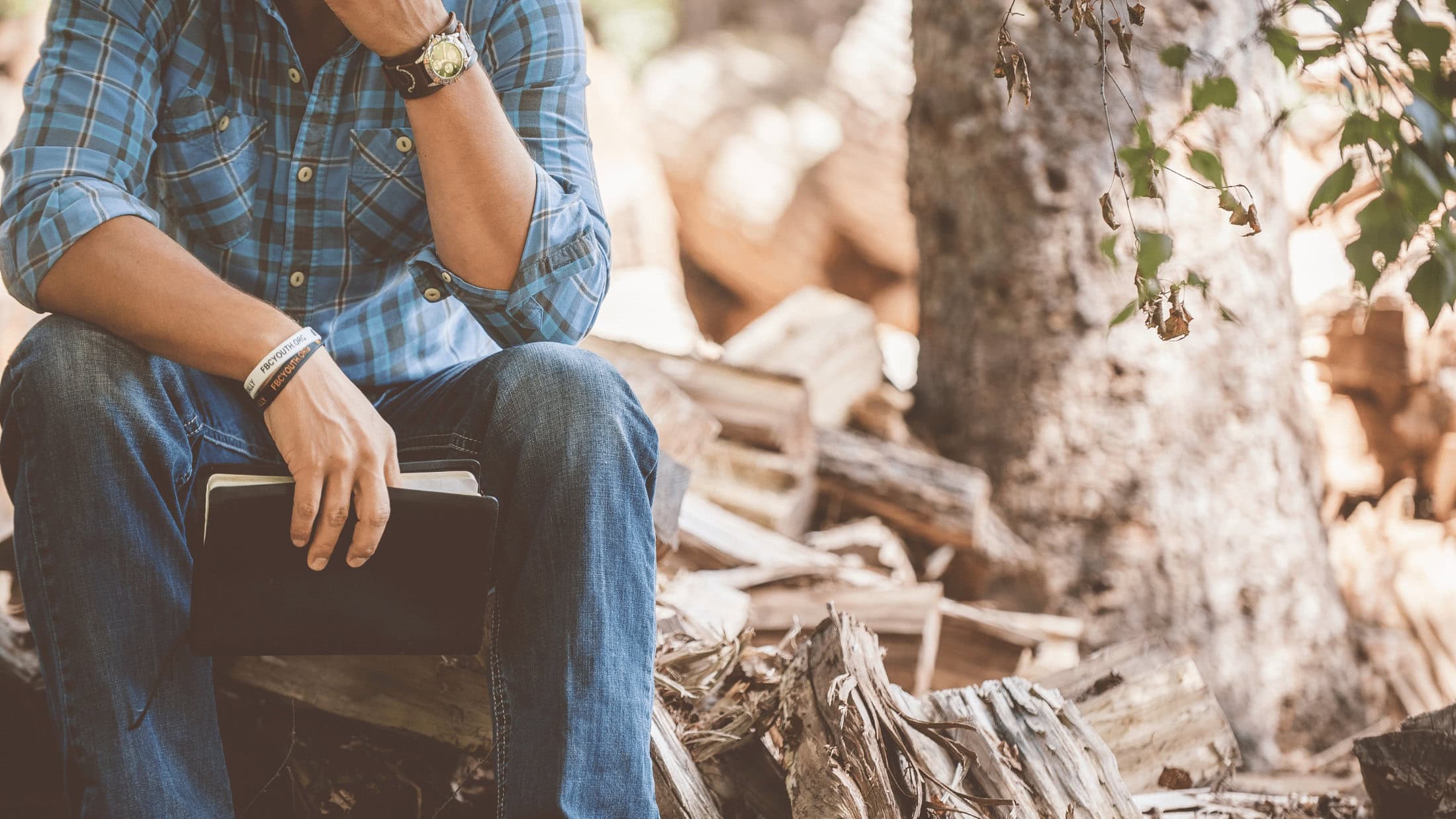 man sitting next to a tree holding a bible