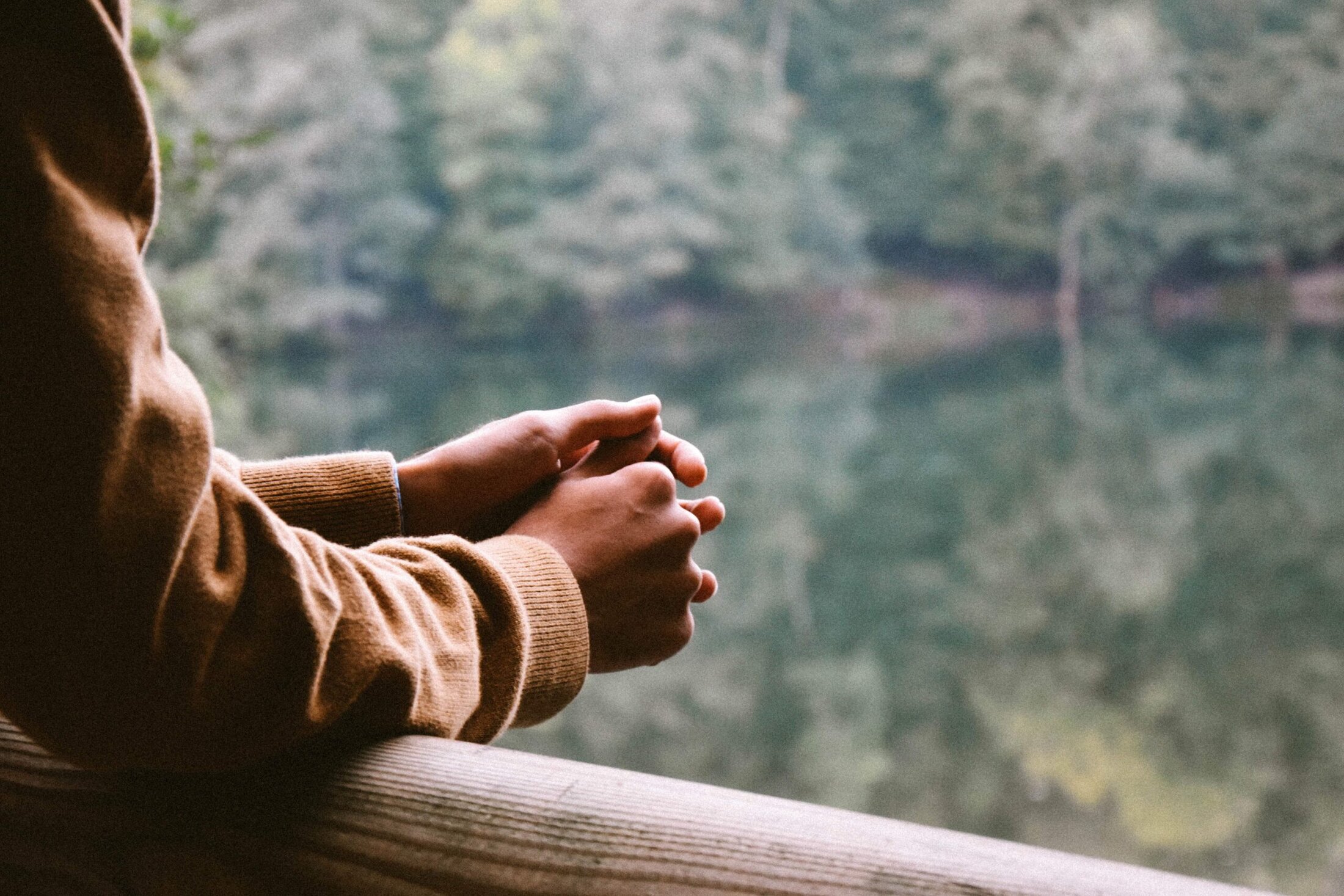 man with crossed hands looking out over lake while wearing brown jacket